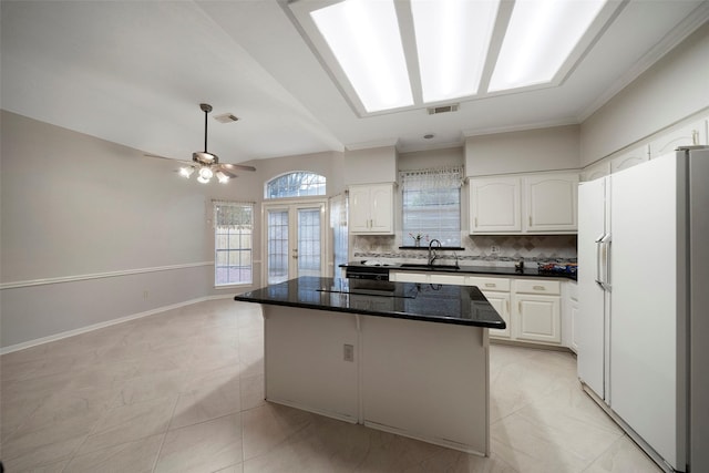 kitchen featuring visible vents, freestanding refrigerator, a sink, white cabinetry, and tasteful backsplash