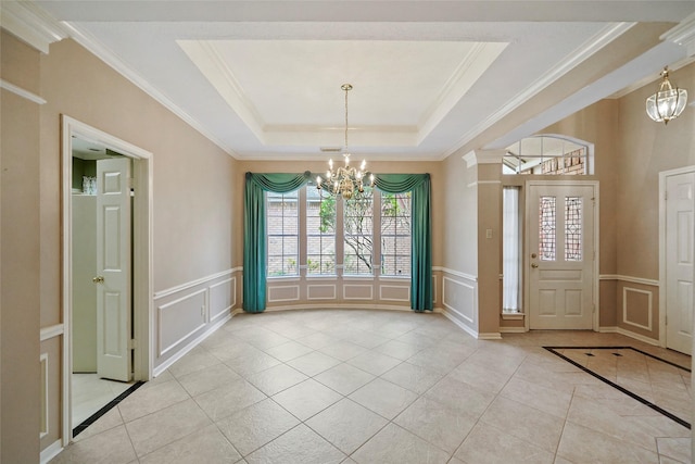 entryway with light tile patterned floors, a tray ceiling, ornamental molding, a decorative wall, and a chandelier