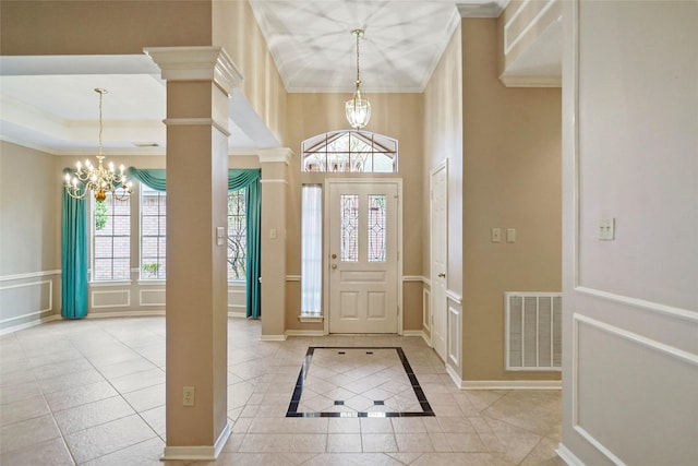 tiled foyer with a notable chandelier, visible vents, crown molding, and a decorative wall