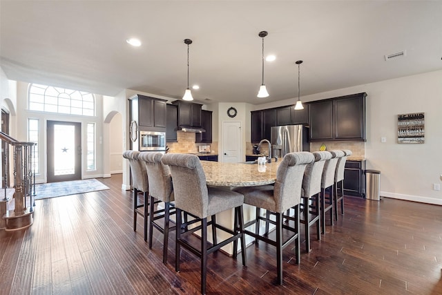 kitchen featuring a kitchen bar, dark wood-style floors, arched walkways, stainless steel appliances, and a sink