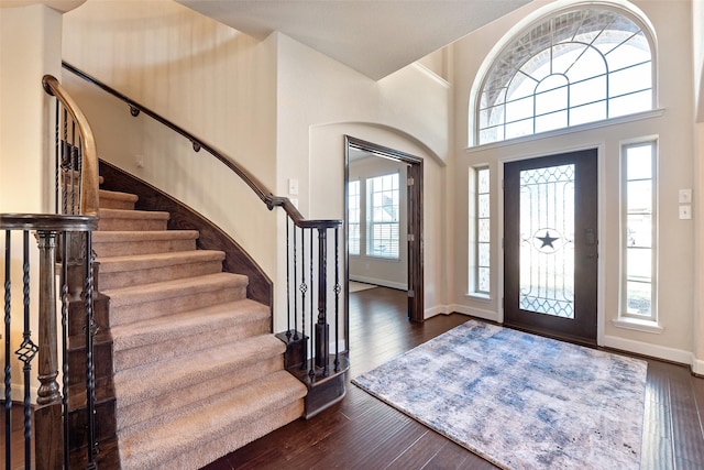 foyer entrance with stairway, baseboards, dark wood-style floors, and a towering ceiling