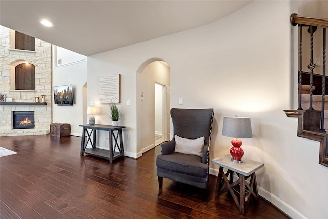 living area featuring a stone fireplace, wood finished floors, arched walkways, and baseboards