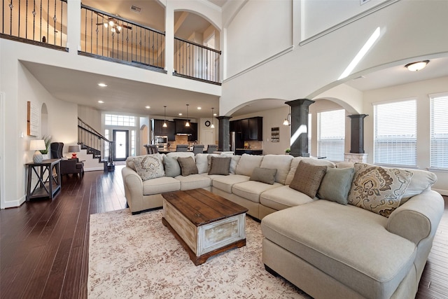 living area featuring stairway, baseboards, visible vents, ornate columns, and hardwood / wood-style flooring