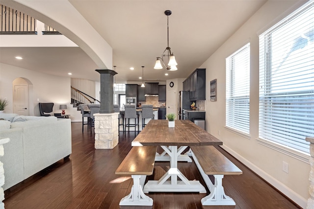 dining area with arched walkways, a notable chandelier, dark wood-type flooring, and baseboards