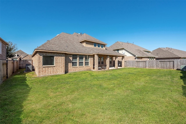 back of property with brick siding, roof with shingles, a lawn, a fenced backyard, and a patio