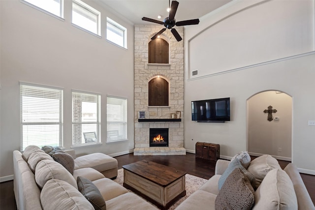 living room featuring baseboards, a stone fireplace, a high ceiling, wood finished floors, and arched walkways