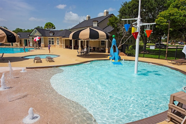 pool with a patio, fence, and a water play area