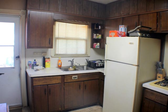 kitchen with dark brown cabinets, light countertops, light tile patterned floors, freestanding refrigerator, and a sink