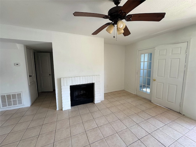 unfurnished living room with light tile patterned floors, visible vents, a brick fireplace, and a ceiling fan