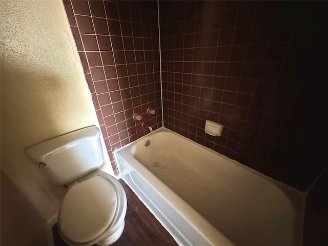 bathroom with toilet,  shower combination, and a textured wall