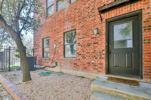 view of exterior entry with brick siding and fence