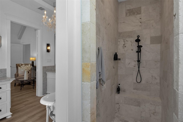 bathroom with visible vents, wood finished floors, a tile shower, tile walls, and a chandelier