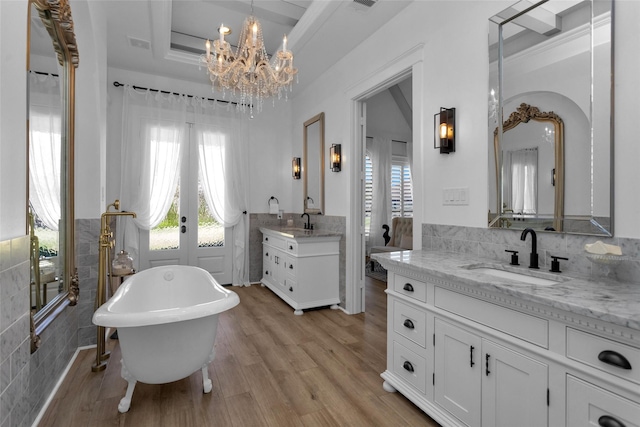 bathroom with wood finished floors, a tray ceiling, two vanities, a sink, and french doors