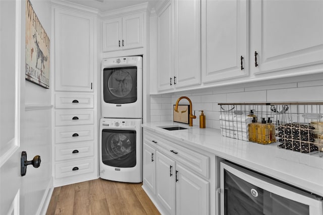 laundry room with stacked washer and dryer, beverage cooler, a sink, cabinet space, and light wood finished floors