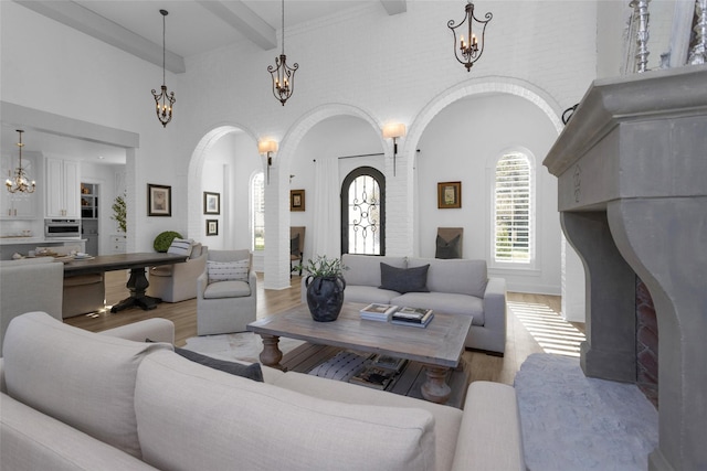 living room with an inviting chandelier, wood finished floors, a fireplace with raised hearth, and beam ceiling