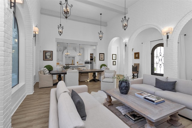 living room featuring wood finished floors, a towering ceiling, arched walkways, brick wall, and a chandelier