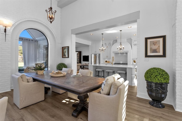 dining space with a notable chandelier, a high ceiling, brick wall, light wood finished floors, and baseboards