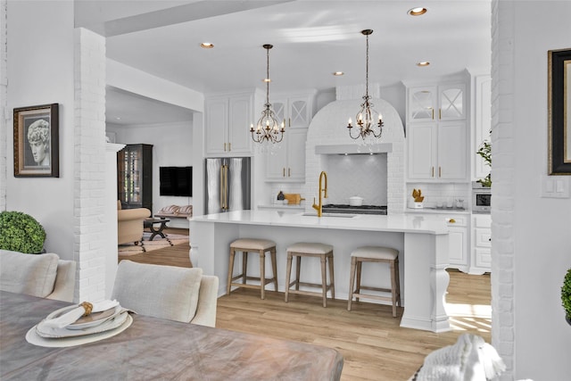 kitchen with light wood finished floors, a breakfast bar area, light countertops, stainless steel fridge, and white cabinetry