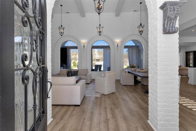 living area featuring beamed ceiling, decorative columns, a high ceiling, light wood-style floors, and arched walkways