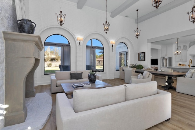 living area with beam ceiling, a notable chandelier, light wood-style floors, and a healthy amount of sunlight