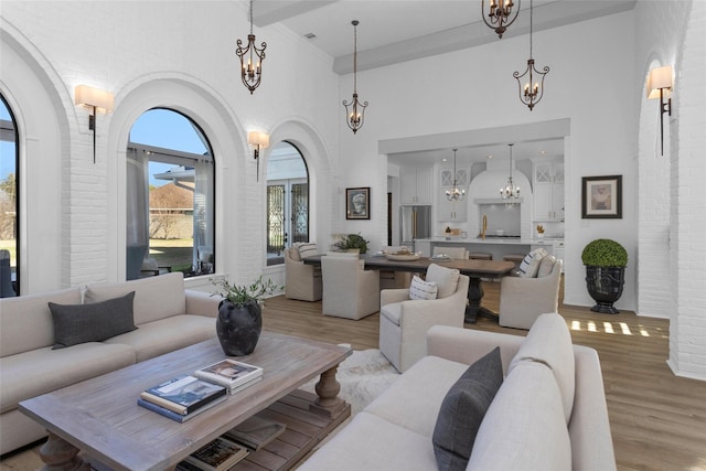 living room featuring brick wall, an inviting chandelier, a high ceiling, arched walkways, and light wood-type flooring