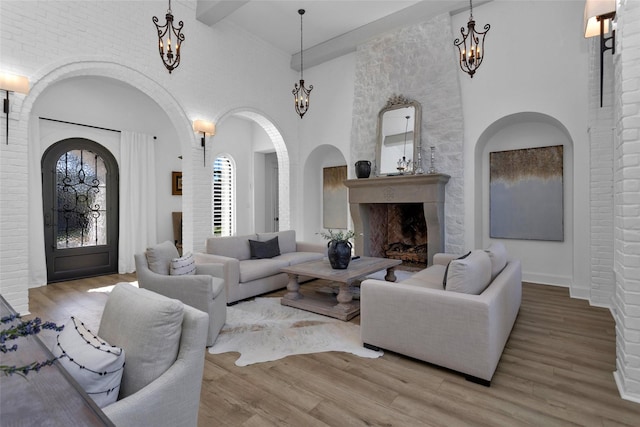 living area with wood finished floors, arched walkways, a fireplace, a chandelier, and a towering ceiling