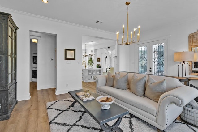 living area featuring light wood-type flooring, stacked washer and clothes dryer, crown molding, and an inviting chandelier