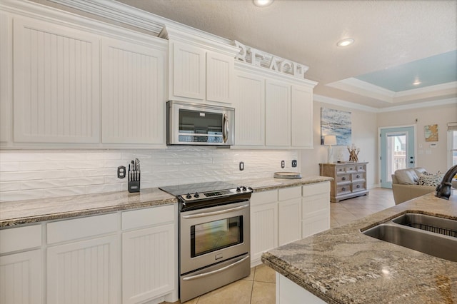 kitchen with a tray ceiling, light tile patterned flooring, ornamental molding, a sink, and appliances with stainless steel finishes