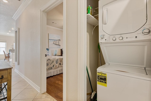 washroom featuring ornamental molding, a textured ceiling, stacked washing maching and dryer, light tile patterned floors, and baseboards