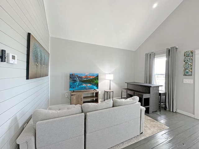 living room featuring baseboards, high vaulted ceiling, wooden walls, and hardwood / wood-style flooring