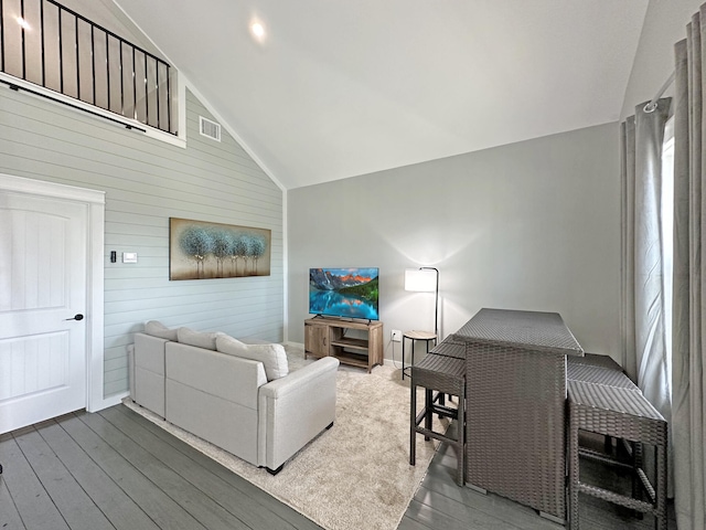 living room with visible vents, wood walls, high vaulted ceiling, and wood finished floors