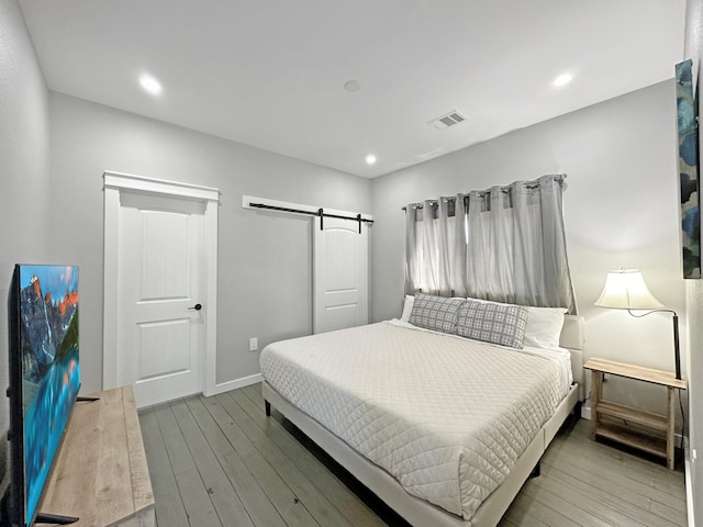 bedroom featuring visible vents, baseboards, a barn door, recessed lighting, and wood-type flooring