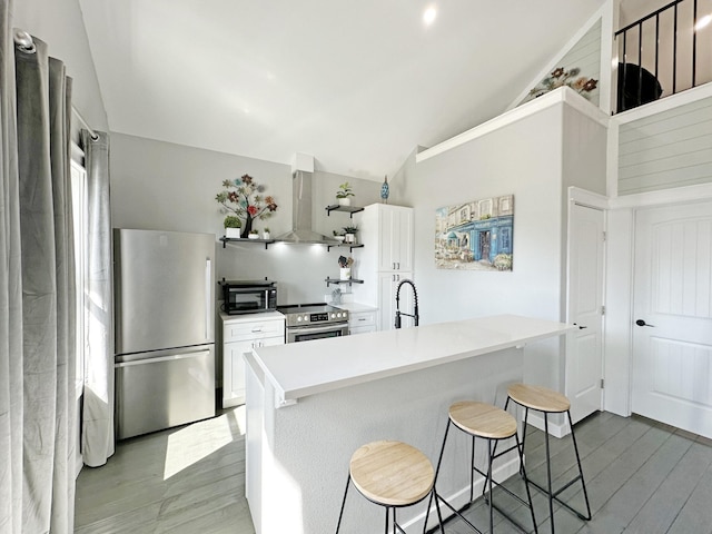 kitchen featuring white cabinetry, appliances with stainless steel finishes, vaulted ceiling, and wall chimney range hood