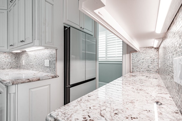 kitchen featuring light stone counters, backsplash, and stainless steel refrigerator