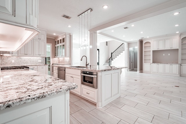 kitchen featuring visible vents, a sink, light stone counters, stainless steel appliances, and crown molding