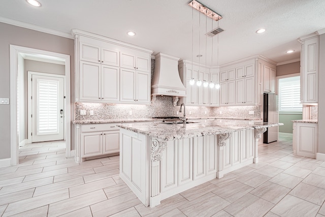 kitchen featuring tasteful backsplash, visible vents, stainless steel fridge, and premium range hood