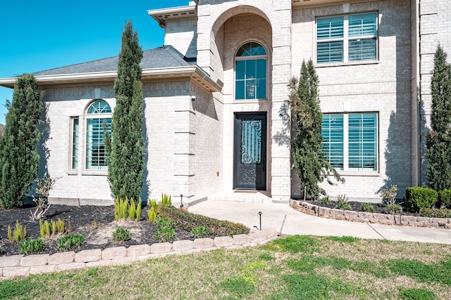 entrance to property with brick siding and a shingled roof