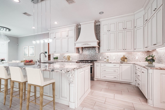 kitchen featuring visible vents, a sink, custom range hood, high end stainless steel range oven, and backsplash