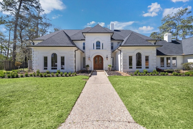 french country style house with french doors, a chimney, a front lawn, and a shingled roof