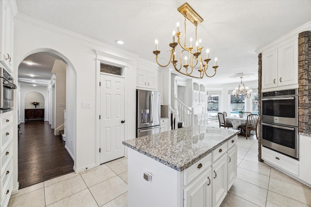 kitchen featuring light stone countertops, light tile patterned floors, stainless steel appliances, an inviting chandelier, and white cabinetry