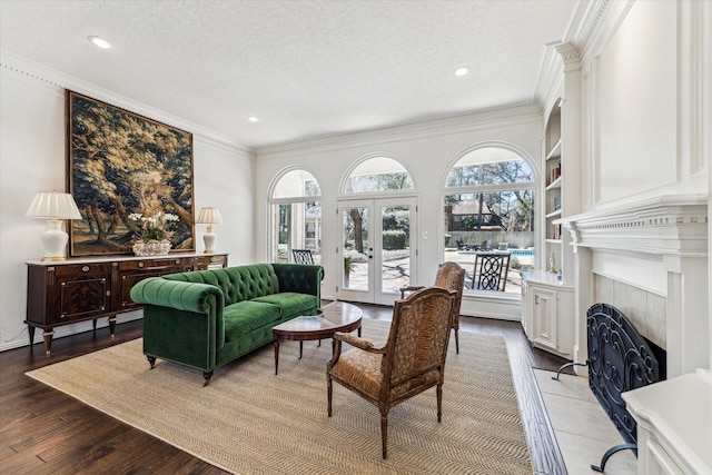 living room featuring wood finished floors, a fireplace, ornamental molding, french doors, and a textured ceiling