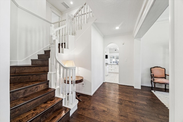 foyer with visible vents, wood finished floors, arched walkways, crown molding, and baseboards