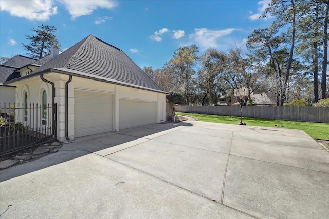 view of side of property featuring fence, a garage, driveway, and a shingled roof