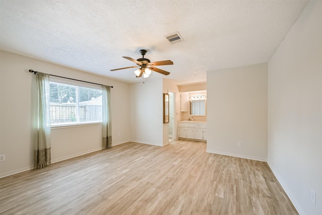 unfurnished room featuring baseboards, visible vents, ceiling fan, light wood-style floors, and a textured ceiling