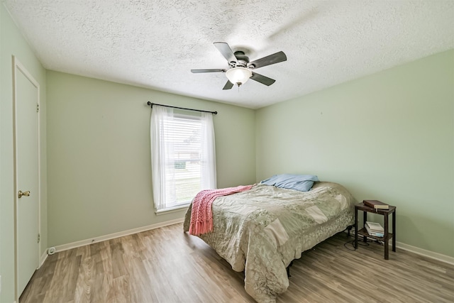 bedroom with a textured ceiling, wood finished floors, baseboards, and ceiling fan