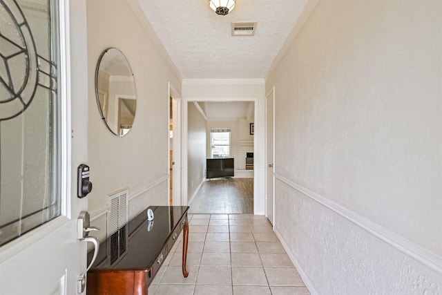 hall featuring light tile patterned floors, visible vents, a textured ceiling, and ornamental molding