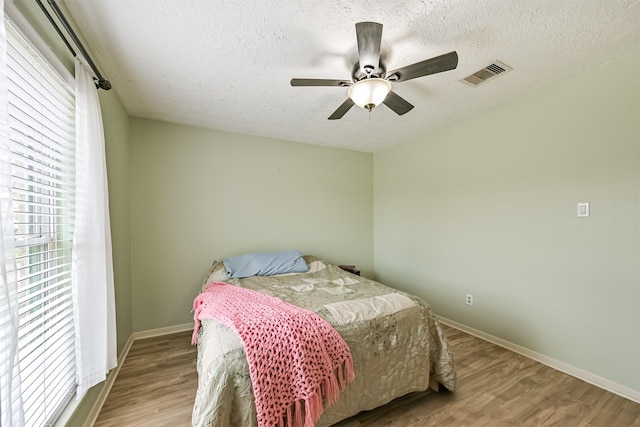 bedroom featuring visible vents, baseboards, a textured ceiling, and wood finished floors