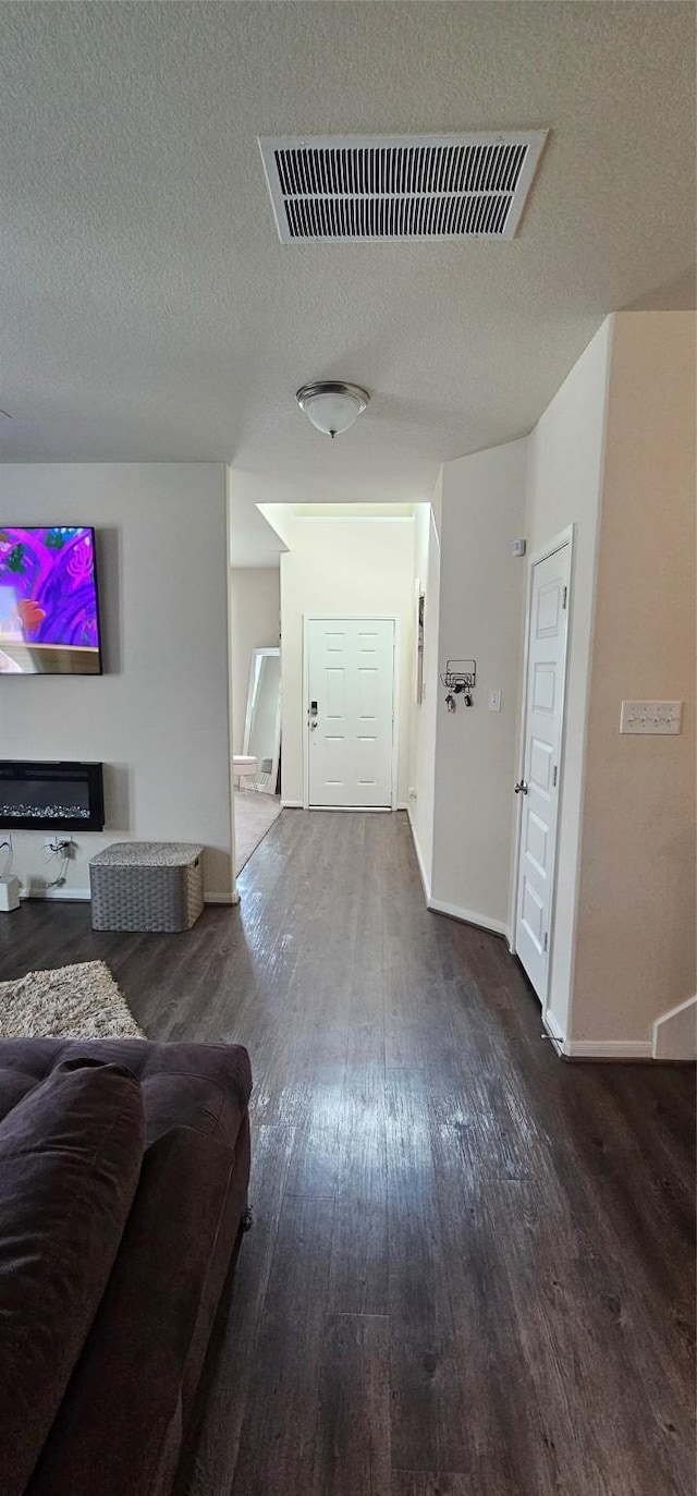 hall with baseboards, wood finished floors, visible vents, and a textured ceiling