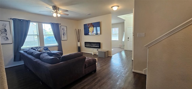 living room featuring dark wood-style floors, a glass covered fireplace, baseboards, and a wealth of natural light