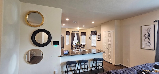 kitchen featuring visible vents, a sink, dark stone countertops, dark wood-style floors, and recessed lighting